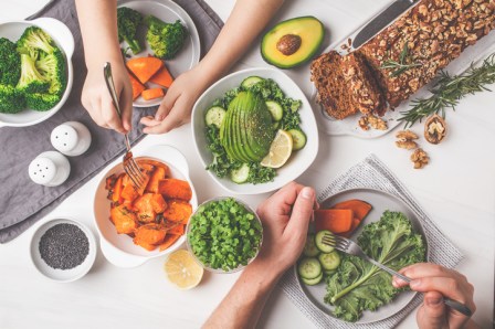 Healthy vegan food lunch, top view. Vegetarian dinner table, people eat healthy food. Salad, sweet potato, vegan cake, vegetables on white background.